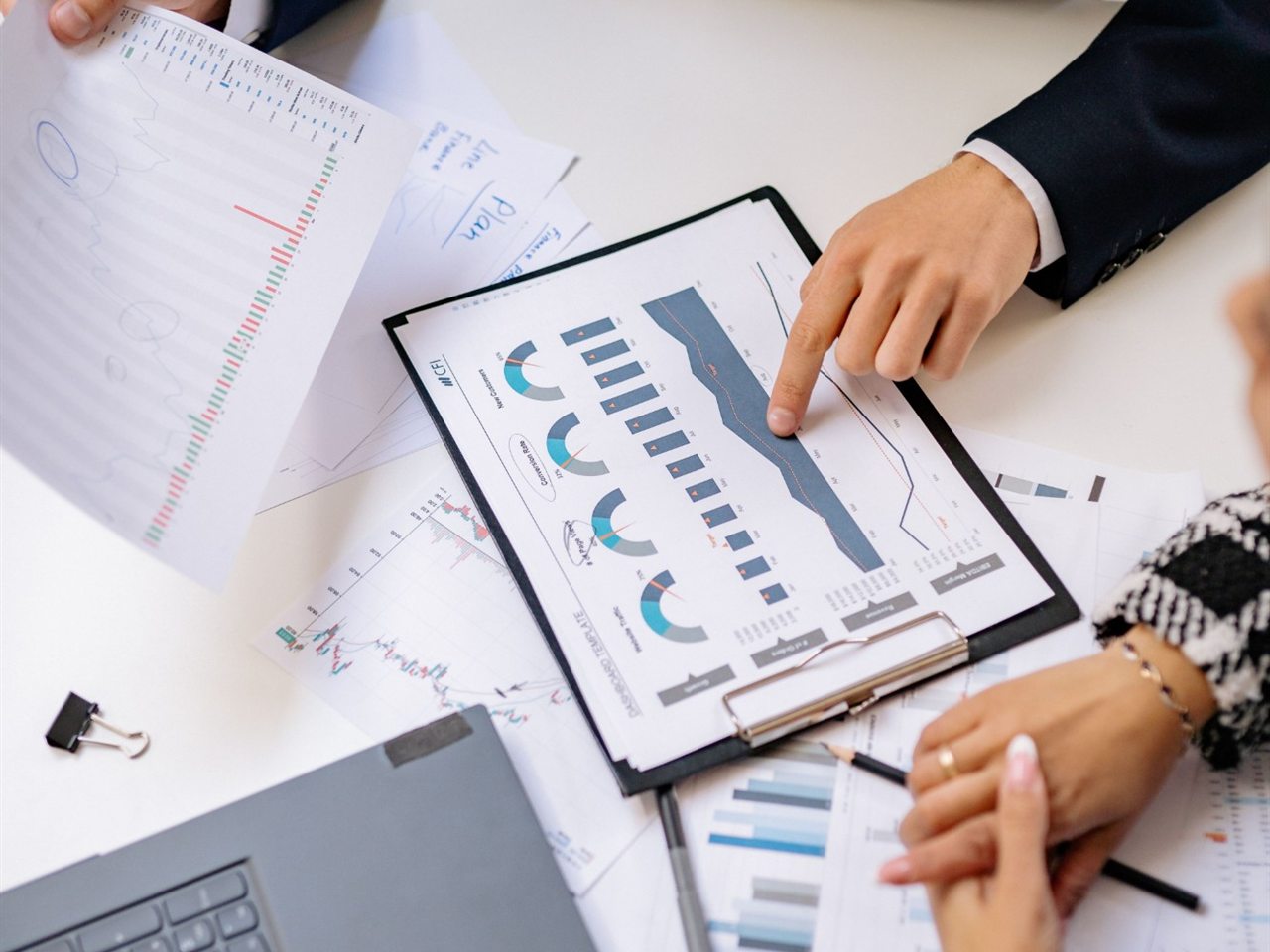 Finanzkennzahlen und Diagramme auf einem Klemmbrett, eine Hand zeigt auf eine Kurve.