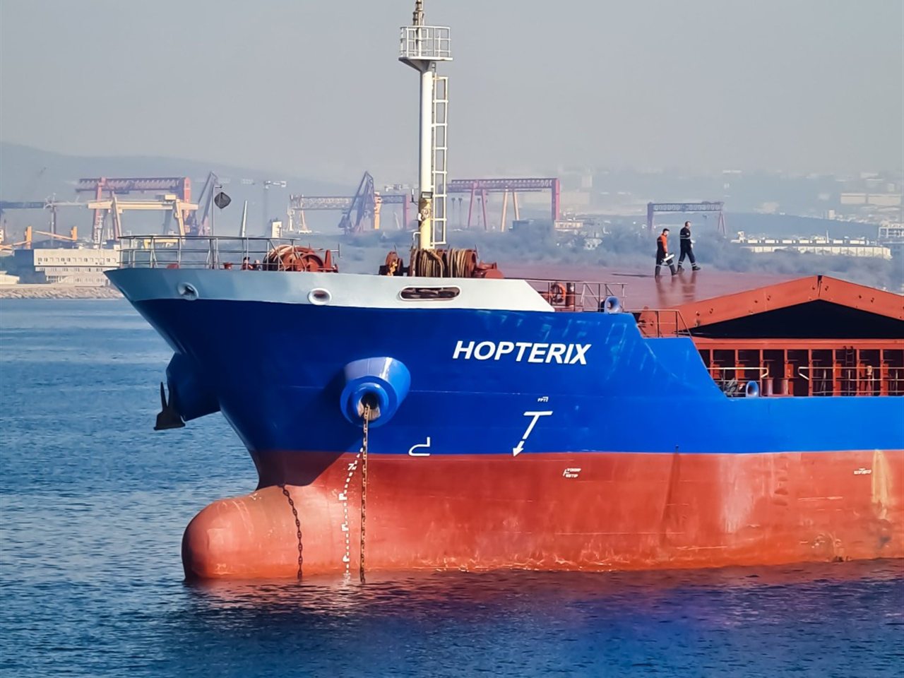 Blauer Frachter mit rotem Rumpf im Hafen vor Hafenkränen.