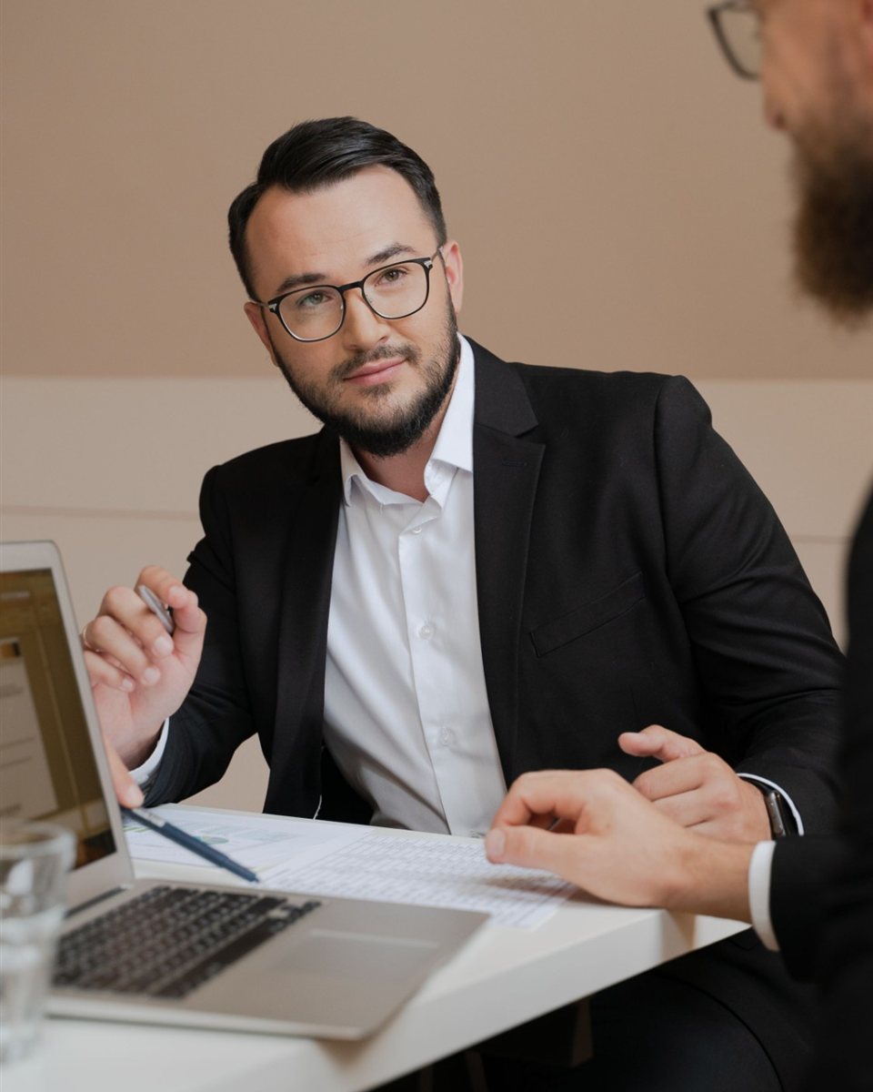 Symbolbild: Mann mit Brille im dunklen Sakko im Fachgespräch am Laptop.